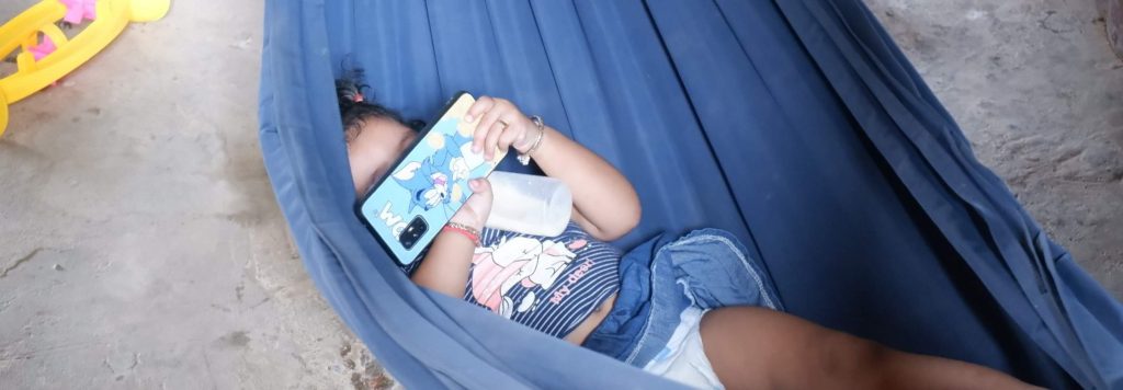Une petite fille en train de prendre son biberon seule, un téléphone dans la main