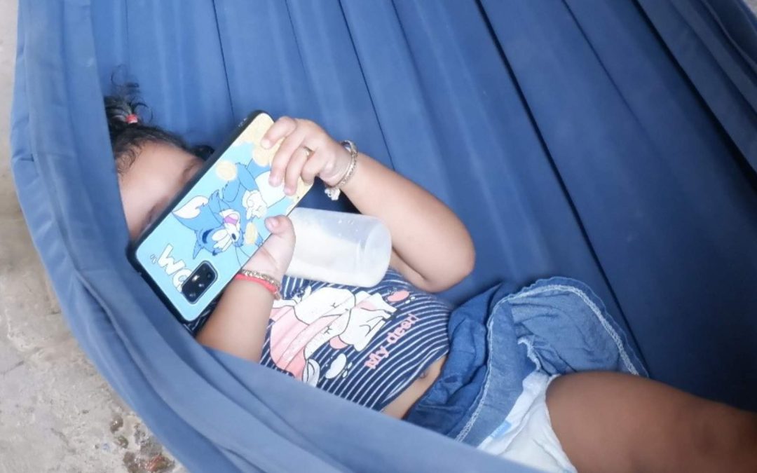 Une petite fille en train de prendre son biberon seule, un téléphone dans la main